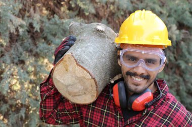 Kasklı yakışıklı oduncunun portresi omuzunda kütük tutuyor.