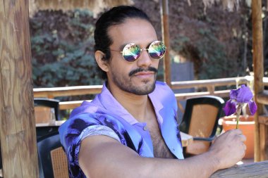 Açık havada orkide çiçekli, şık, mor gömlekli genç bir adamın portresi.