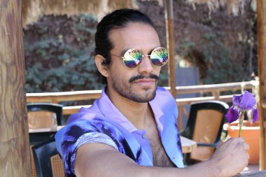 Açık havada orkide çiçekli, şık, mor gömlekli genç bir adamın portresi.