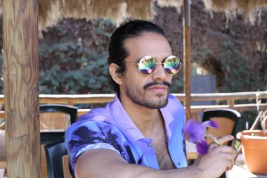 Açık havada orkide çiçekli, şık, mor gömlekli genç bir adamın portresi.