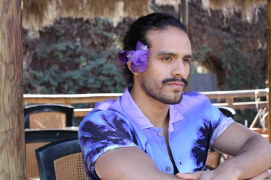 Açık havada orkide çiçekli, şık, mor gömlekli genç bir adamın portresi.