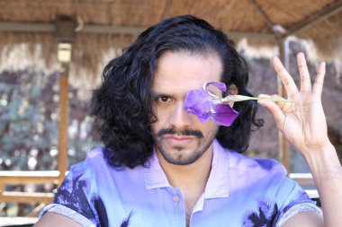 Açık havada orkide çiçekli, şık, mor gömlekli genç bir adamın portresi.