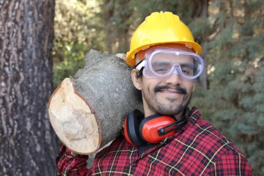 Kasklı yakışıklı oduncunun portresi omuzunda kütük tutuyor.