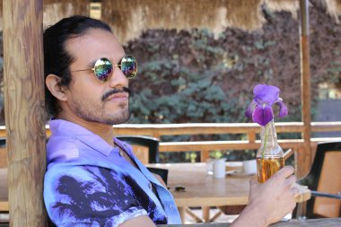 Açık havada orkide çiçekli, şık, mor gömlekli genç bir adamın portresi.