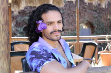 Açık havada orkide çiçekli, şık, mor gömlekli genç bir adamın portresi.