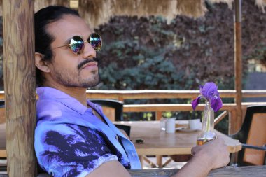 Açık havada orkide çiçekli, şık, mor gömlekli genç bir adamın portresi.