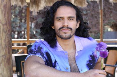 Açık havada orkide çiçekli, şık, mor gömlekli genç bir adamın portresi.