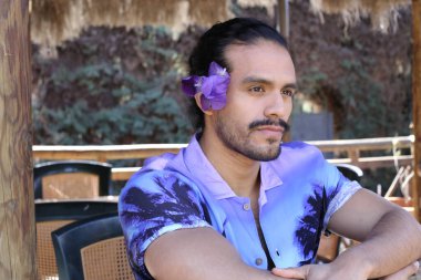 Açık havada orkide çiçekli, şık, mor gömlekli genç bir adamın portresi.