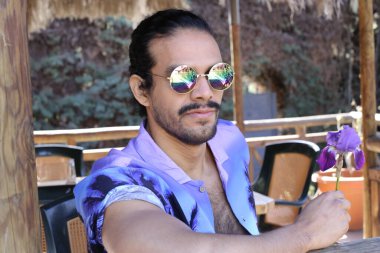 Açık havada orkide çiçekli, şık, mor gömlekli genç bir adamın portresi.