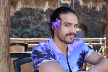 Açık havada orkide çiçekli, şık, mor gömlekli genç bir adamın portresi.