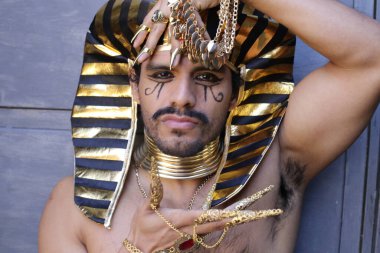 Gri duvarda altın rengi Mısır firavunu kostümlü yakışıklı genç adam portresi.