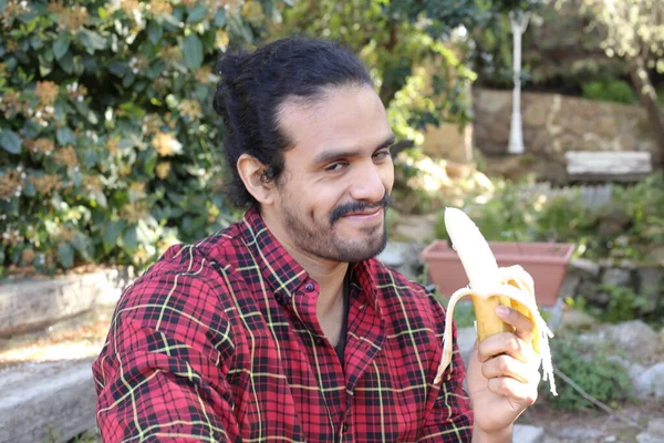 バナナを屋外で食べるハンサムな若い男の肖像画 — ストック写真