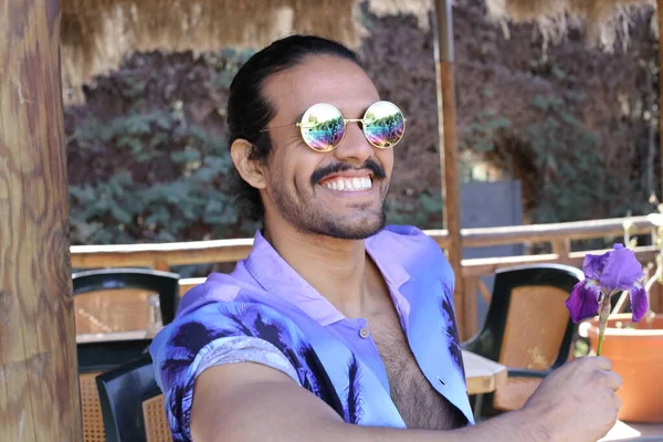 Açık havada orkide çiçekli, şık, mor gömlekli genç bir adamın portresi.