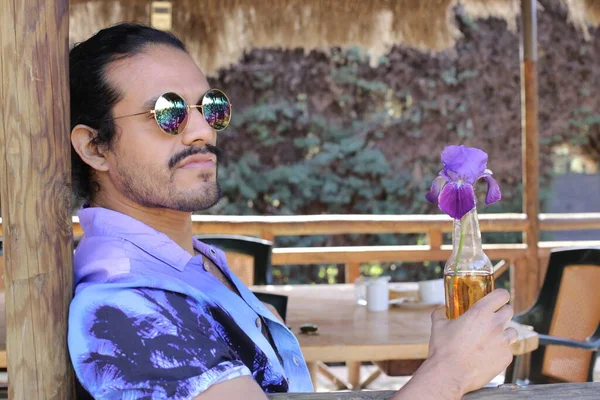 Açık havada orkide çiçekli, şık, mor gömlekli genç bir adamın portresi.