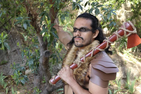 portrait of handsome young man in fantasy barbarian armor with axe in forest