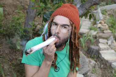 Uzun rastalı yakışıklı genç adamın yakın plan portresi doğada dev ot otları tutuyor.