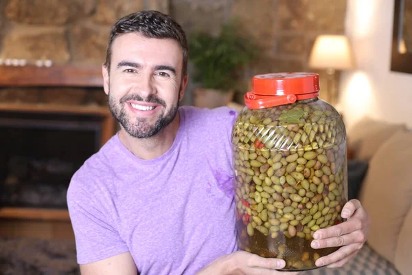 close-up portrait of handsome young man with giant jar with olives at home