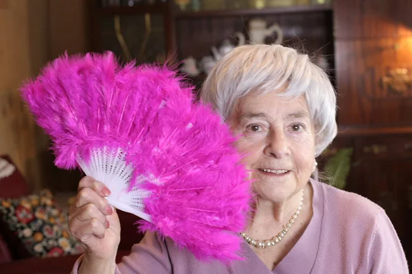 自宅でピンクの羽を持つハンドヘルドファンを持つ成熟した女性のクローズアップ肖像画 — ストック写真