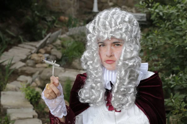 portrait of young woman in Victorian wig and dress smoking cigarette outdoors in park