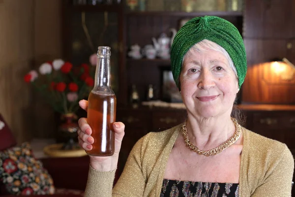 自宅でビールのグラスボトルを持っている緑の帽子の成熟した女性のクローズアップ肖像 — ストック写真