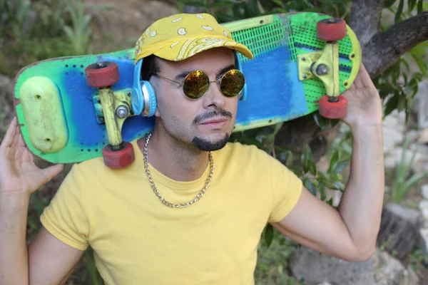 公園に立ってカラフルなスケートボードを持つハンサムな若い男のクローズアップ肖像画 — ストック写真