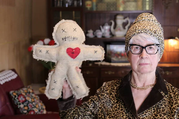 自宅でブードゥー教の人形を保持帽子とヒョウのジャケットで成熟した女性のクローズアップ肖像 — ストック写真
