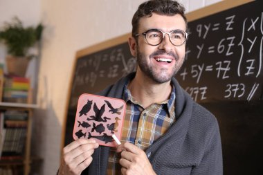 Sınıfta tahtada balık ve kuş siluetleriyle şablon tutan yakışıklı bir öğretmenin yakın plan portresi.