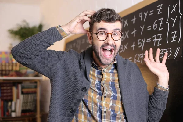 close-up portrait of funny young teacher grimacing in front of blackboard in classroom