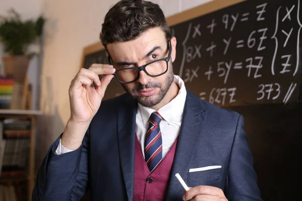 教室の黒板の前でチョークを持ってスーツ姿のハンサムな若い先生のクローズアップ肖像画 — ストック写真