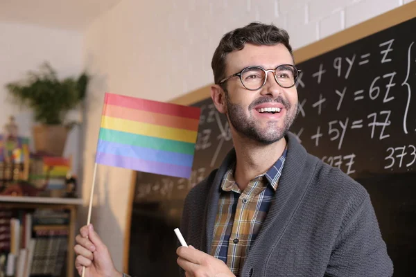 Igbtq bayrağını sınıfın tahtasının önünde tutan yakışıklı genç öğretmenin yakın plan portresi.