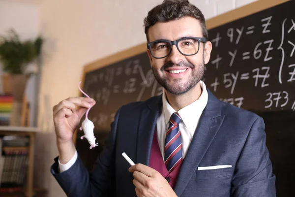 close-up portrait of handsome young teacher with chalk and white mouse in front of blackboard in classroom