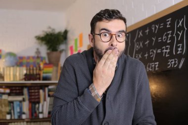 Sınıfın tahtası önünde şok olmuş genç bir öğretmenin yakın plan portresi.