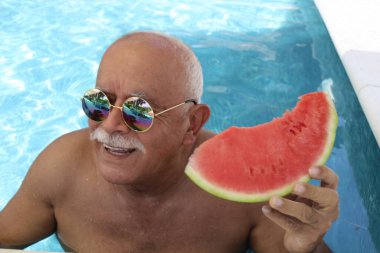 Güneşli yaz gününde havuzunda bir dilim karpuzla olgun bir adamın portresi.