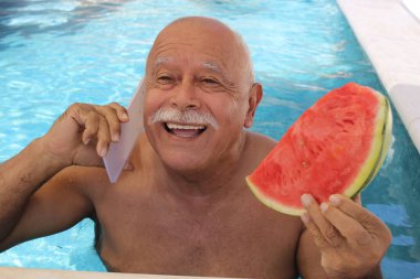 Olgun bir adamın portresi bir dilim karpuzla güneşli bir yaz gününde bilardoda telefonla konuşuyor.