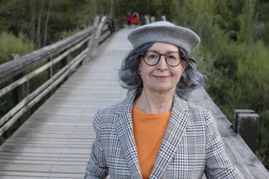 Güzel olgun bir kadının yakın plan portresi. Açık havada, ahşap köprüde şık kıyafetler içinde.