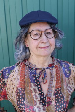 Yeşil duvarın önünde şık giyinmiş güzel olgun bir kadının yakın plan portresi.