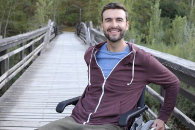 Parktaki ahşap köprüde tekerlekli sandalyedeki yakışıklı genç adamın portresi.