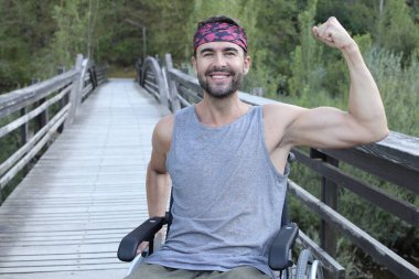 Parktaki ahşap köprüde tekerlekli sandalyedeki yakışıklı genç adamın portresi.