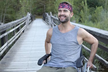 Parktaki ahşap köprüde tekerlekli sandalyedeki yakışıklı genç adamın portresi.