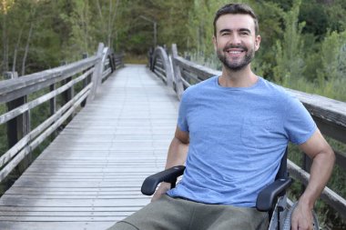 Parktaki ahşap köprüde tekerlekli sandalyedeki yakışıklı genç adamın portresi.