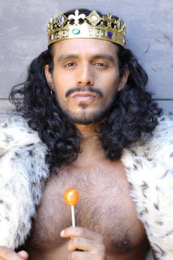 Kral pelerinli ve elinde lolipop tutan yakışıklı melez bir adamın yakın plan portresi.