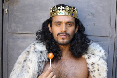 Kral pelerinli ve elinde lolipop tutan yakışıklı melez bir adamın yakın plan portresi.