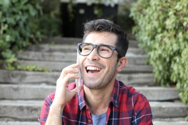 Yakından çekilmiş, sıradan kıyafetler içinde, merdivenlerde oturmuş telefonla konuşan yakışıklı bir genç portresi.