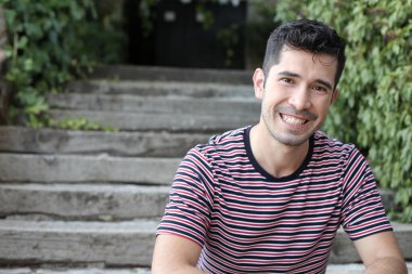 Yakından çekilmiş, sıradan giysiler içinde merdivenlerde oturan yakışıklı bir genç portresi.