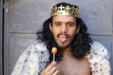 Kral pelerinli ve elinde lolipop tutan yakışıklı melez bir adamın yakın plan portresi.