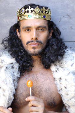 Kral pelerinli ve elinde lolipop tutan yakışıklı melez bir adamın yakın plan portresi.
