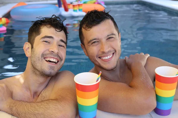 happy young gay couple enjoying their time together in pool with paper cups in colors of lgbtq flag
