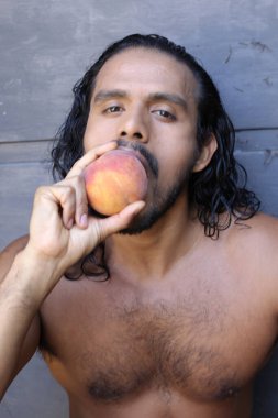 Yakışıklı, genç, melez bir adamın beton duvarın önünde şeftali yerken çekilmiş portresi.