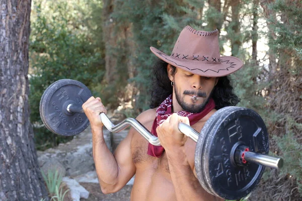 森林里戴牛仔帽 拿着杠铃锻炼的年轻英俊 赤身裸体男子的特写 — 图库照片