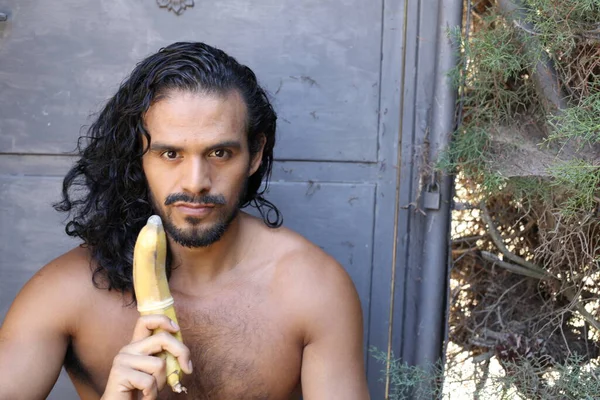 年轻英俊的混血儿 赤身裸体 拿着带避孕套香蕉的男子的特写 — 图库照片